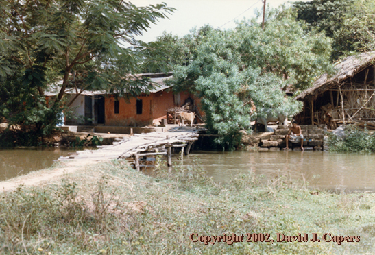 A man sits reflecting beside the water in his village of birth.